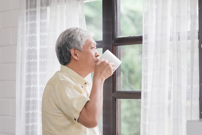 happy asian elderly man smiling drinking cup coffee tea near window living room senior asia male open curtains relax morning